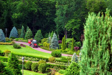 Kirpik çalılar ve hedges, yeşil çim ve ağaçların bitkilerin bakımı için bir bahçıvan traktör ile köşkün arka bahçe peyzaj tasarımı.