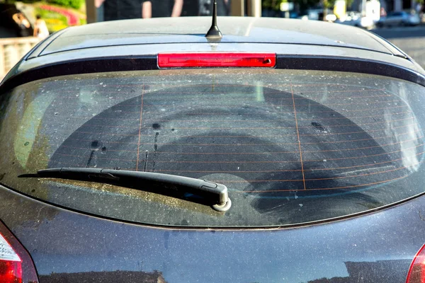 Dirty car rear window, car wagon covered with dust outside in sunny, close-up rear window with car wiper.