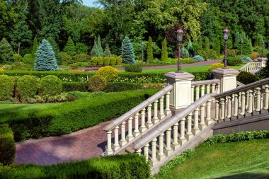 Merdiven korkuluk korkuluk ve retro bir fener bir kaide üzerinde bir landscaped park ve Bahçe çitleri ve diğer bitkiler ile bir geçit altına iner.