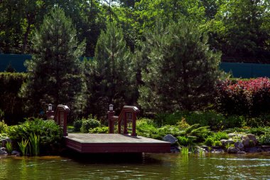 Bir İskelesi ahşap döşeme arka planda havuz korkuluk ile yeşil ağaçlar ve çalılar ile bir manzara olduğunu.