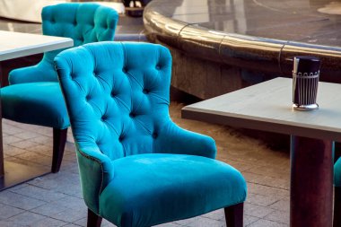 upholstered armchair with fabric covering at the square wooden table on the stone tiles of the street cafe.