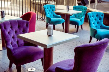 kare beyaz masalar ve taş döşeme levhalar üzerinde çok renkli yumuşak tekstil sandalyeler ile açık kafe.