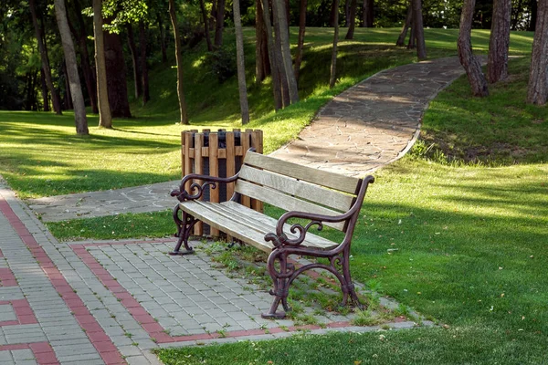 木の座席と鍛造鉄の脚舗装スラブ緑の風景やバック グラウンドでの石の道が付いている木の木製ゴミ箱ベンチ — ストック写真