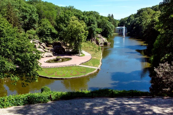 Bir su birikintisi ve flowerbed taş kayalıklarla ve park rekreasyon için yüksek yeşil ağaçlar arasında Park.