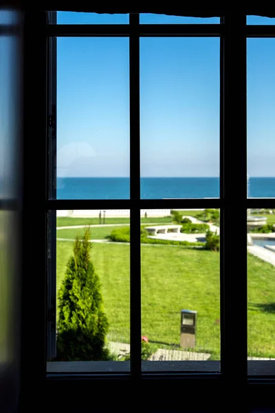 window frame from the inside of the room with a lawn and a view of the sea visible in the backyard of the mansion.