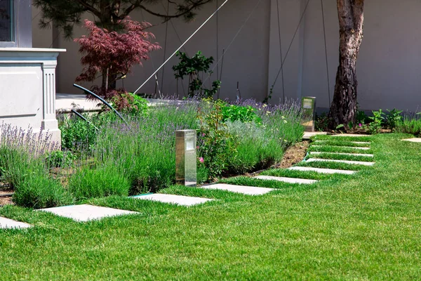 güneşli bir yaz gününde yeşil çim kare mermer fayans yapılmış bir çiçek tarhı ve taş yolu ile lüks bir konak arka bahçesinde.