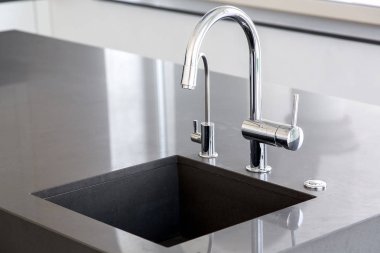 parlak bir çalışma yüzeyi ile temiz bir mutfakta krom musluk ile koyu gri taş mutfak lavabo, musluk lavabo kadar yakın.