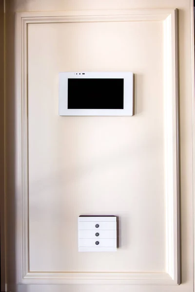 Smart home control system, Controls the functionality of the system, a touchscreen tablet with a screen and a white touchscreen switch buttons mounted on a beige wall.