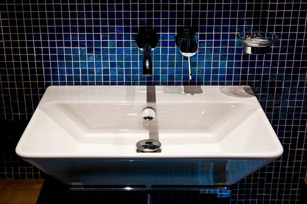 青いモザイクの壁が付いている浴室の鉄の蛇口が付いている白い陶磁器の洗面器 — ストック写真