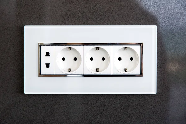 socket with plugs for standard type A plug and standard type F plug in white plastic case on a dark gray glossy stone wall.