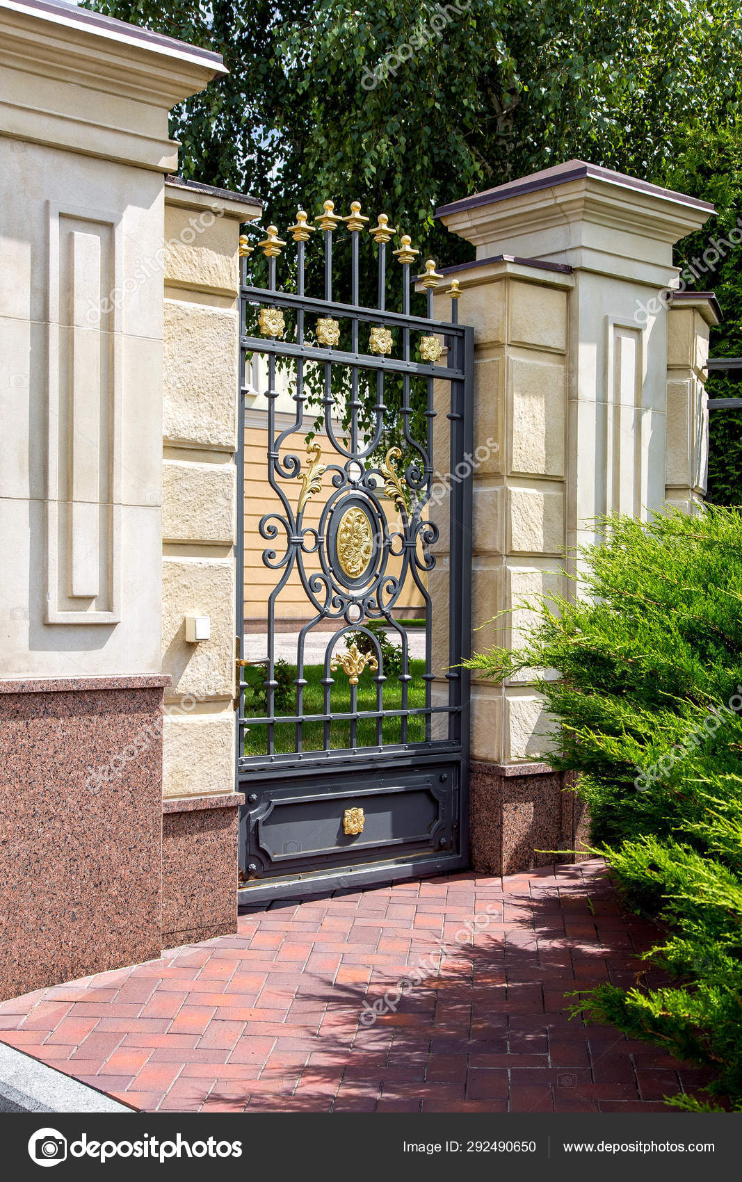 鉄製の鉄門は 首都の石垣と木々の庭とタイルの歩道に沿って緑のthujaと邸宅の領土への入り口 ストック写真 C Bespaliya