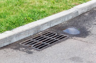 yağmur ve yeşil çim sonra su birikintisi ile drenaj sistemi ile rögar ızgara ile asfalt yol.