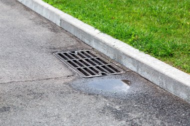 yağmurdan sonra bir su birikintisi ile asfalt yolda drenaj sisteminin rögar ızgara.