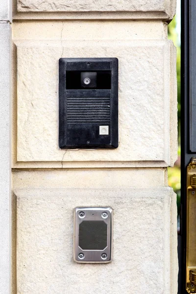 An intercom with a call button and a camera with a microphone on a stone wall with a rusticate on the bottom of the card reader for access.
