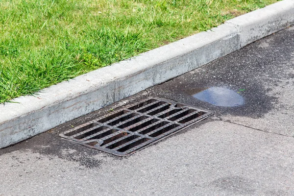 yağmur ve yeşil çim sonra su birikintisi ile drenaj sistemi ile rögar ızgara ile asfalt yol.