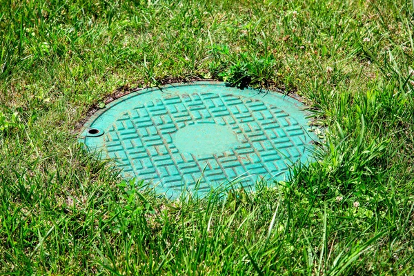 Green iron hatch of a sewer system in a clearing with green grass, close up manhole.