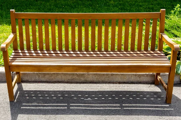 ボードで作られた木製の茶色のベンチは 公園の緑の芝生と縁石の近くのアスファルト舗装に立っています — ストック写真