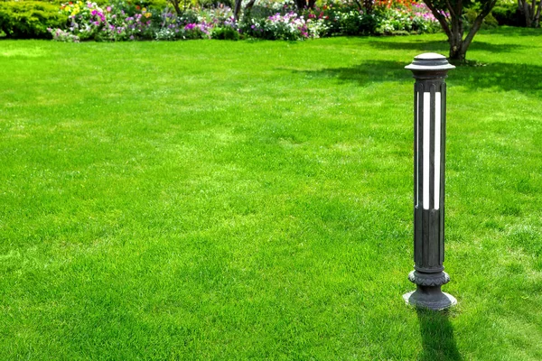 Iron outdoor garden lighting lantern on a green lawn with grass with copy space for text in the background flower beds with flowers.