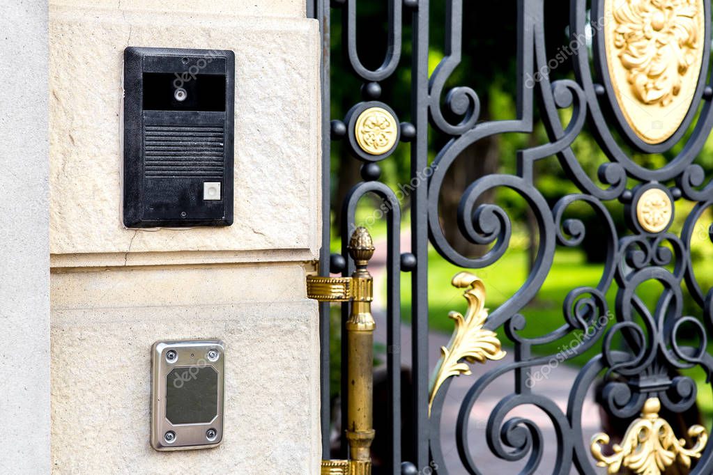 intercom with camera and card reader on the wall near the iron gate forged with a pattern.