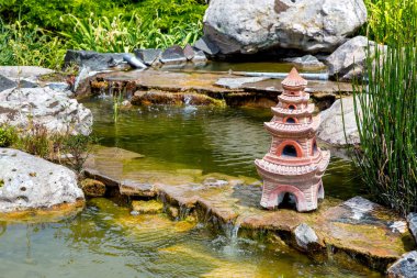 şelale akışı ve suda bir Japon tarzı evin bir taş heykel ile yapay gölet.