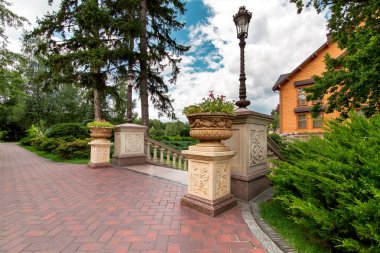 kaldırım ve ağaçlar ve çalılar arasında taş çiçek vazove sokak lambaları ile kaideler ile bir günlük evin arka bahçesinde turistik park.