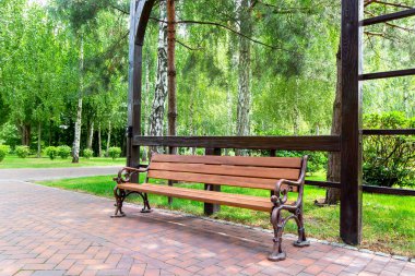 yeşil bir çim ve yürüyüş yolları boyunca ağaçlar ile bahçede bir pergola kemer altında bir tahta dan demir bacaklar ve ahşap bir koltuk ile bir bank.