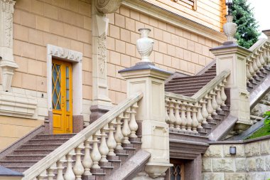 granit merdivenli ve taş korkuluklu, kaideler üzerinde taş vazolar ve yapının diğer mimari detayları ile binanın cephesi.