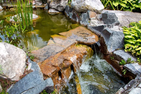 bir gün parkta akış suyu ile taş yapay gölet üzerinde şelale, closeup.