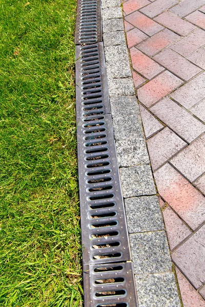 iron grate of a drainage system for storm water drainage from a pedestrian footpath near a green lawn.