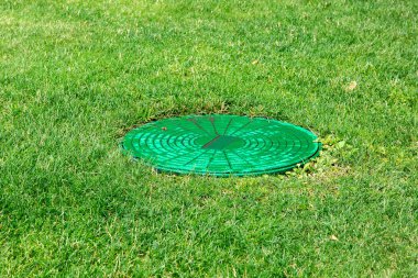 Yeşil çayırda bir kanalizasyon sisteminin yeşil kapak, çim üzerinde rögar kapatın.