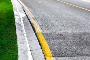kanal akan yağmur suyu sarı işaretler ve bulutlu bir günde yağmurdan sonra yeşil bir çim ile bir asfalt yol kenarında bir drenaj sisteminin bir çimento hendek.