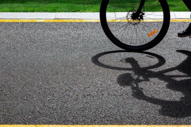 Bir bisiklet tekerleği bir asfalt yol boyunca sürmek ve kopya alanı ile güneşli bir yaz gününde sarı işaretler ile karayolu üzerinde, bir gölge döküm.