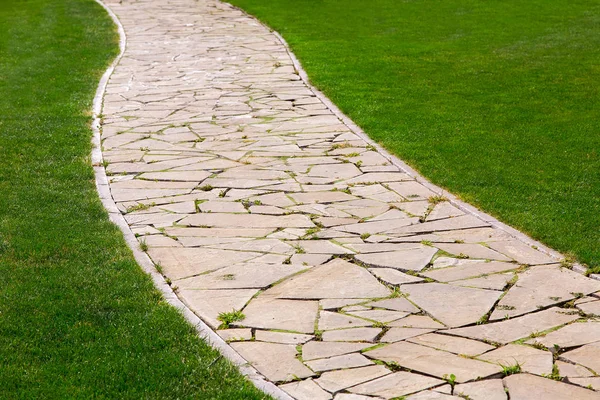 Kaldırımlı ve yeşil çimenli bir parktaki bir desenle döşenmiş farklı taş parçalarından gelen patika..