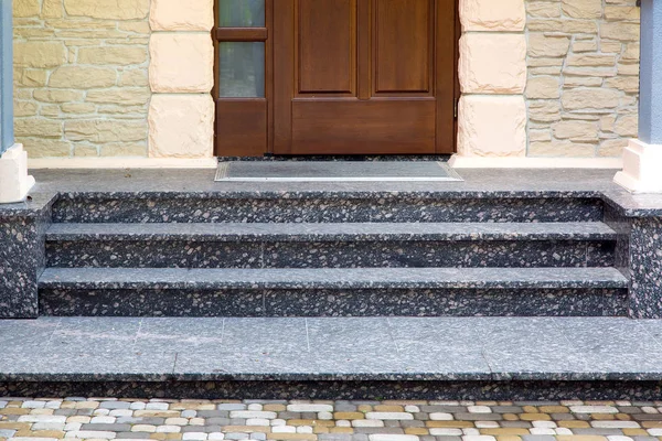 entrance threshold with marble steps to a wooden door with a rubber mat and a stone facade and rustication.