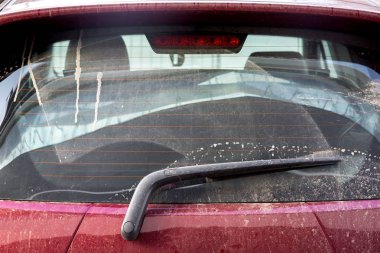 Isıtmalı camların arkasında fren lambası olan tozlu kırmızı bir arabanın arka camı kirli bir arabanın yakın çekimi..