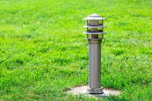 太陽の光で照らされた芝生の緑の芝生の上に電球と地上鉄街灯電気ランプ — ストック写真