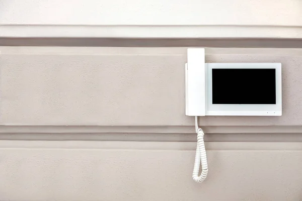 internal intercom with a handset for conversation and a video surveillance screen in a white body is suspended on the wall, closeup of a home security and communication device with copy space.