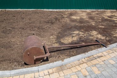 Yuvarlanan toprak için bahçe silindiri Taştan kiremitlerin yakınındaki güneşli bir günde pürüzlü zeminde uzanan demir bir alet, peyzaj tasarım sürecinin yakın çekimi hiç kimsedir.