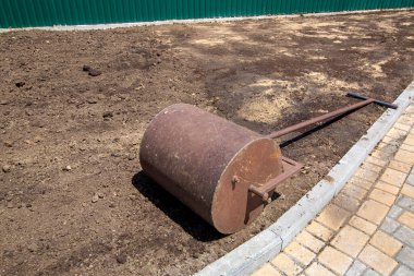 Toprağın sıkıştırılması için bahçe silindiri. Güneşli bir günde yuvarlanan demir bir şaft yerde uzanır. Manzara tasarım sürecine yakın durur..