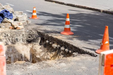 Yol onarım çukuru turuncu koni ile çevrili, asfalt asfalt kaldırım ve kaldırım taşlarıyla yolu kazın.