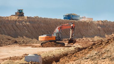 Bir drenaj sistemi kazıcısı inşa etmek için inşaat ekipmanı bir hendek çukuru kazar ve açık havada bir buldozer ile kaldırılan toprak tabakasını çıkarır..