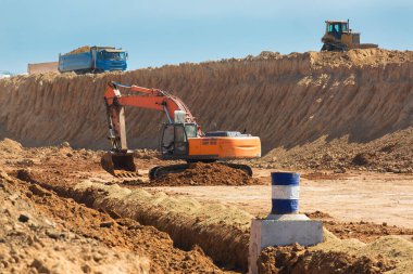 Bir drenaj sistemi kazıcısı yapımında kullanılan inşaat ekipmanları bir hendek çukuru kazıyor ve bir buldozer ile kaldırılan toprak tabakasını çıkarıyor..