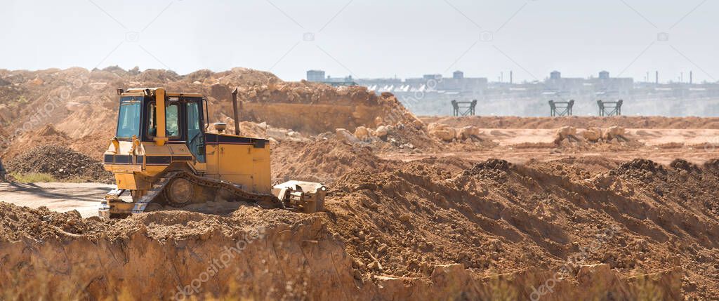 bulldozer heavy machinery transport raking clay for landscape planning before construction, yellow crawler tractor doing work moving earth, nobody.