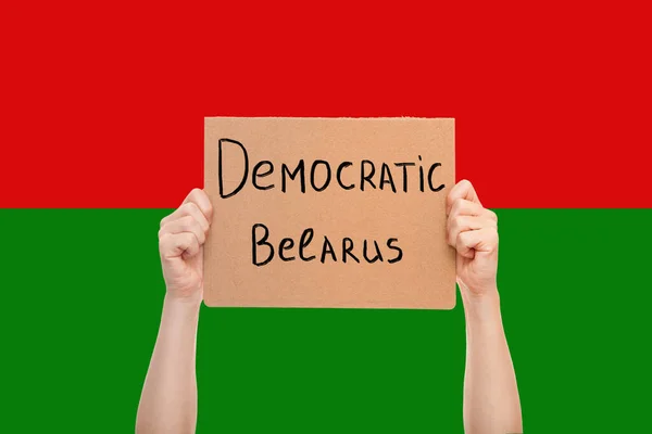 protest poster in hands of free person with message Democratic Belarus, strike against the dictatorial elections in Minsk, hands with cardboard box against the background of national flag.