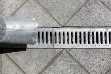 Mühendislik yapısı yağmur suyunu boşaltmak için kanalizasyon ızgarası olan bir drenaj borusu kare karolardan yapılmış granit kaldırımın arka planına karşı..