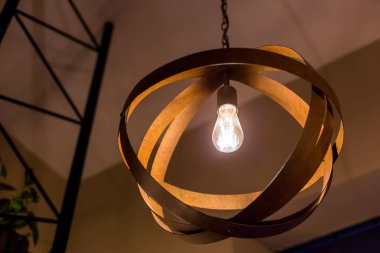 Kolye, ahşap daireler şeklinde bir top şeklinde, parlak bir Edison ampulü, sıcak bir ışıkla parıldıyor, bir kafenin içinde akşam vakti yakın plan, kimse yok..