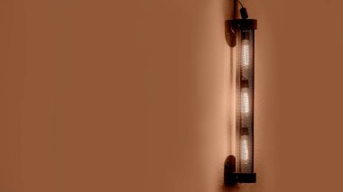 Ilık bir ışıkla parlayan ağ tüpü şeklinde demir bir fener, fotokopi duvarlı bir restoran dekorunun akşam objesi..