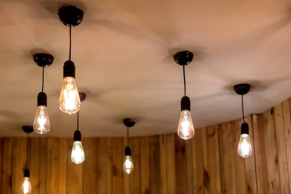 many edison bulbs hanging on a white ceiling in a room with wooden walls, retro style electric lighting in an eco friendly interior close-up of glow details, nobody.