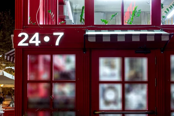 entrance to the red store with a canopy above the door with a luminous signboard 24/7 round the clock shop in the English style of red architecture, close up night scene  nobody.