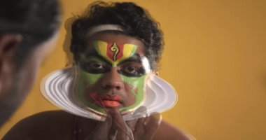 Chuttikaran Kathakali dansçısının yüzüne kırmızı renk uyguluyor.